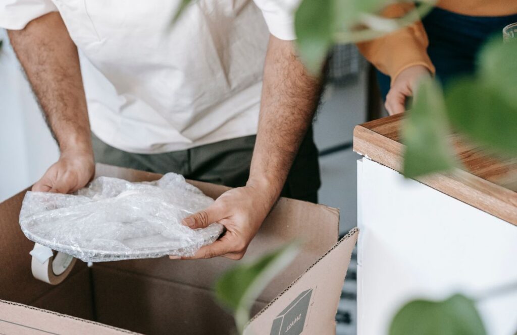 Hands wrapping a dinner plate in packing paper before placing it in a moving box