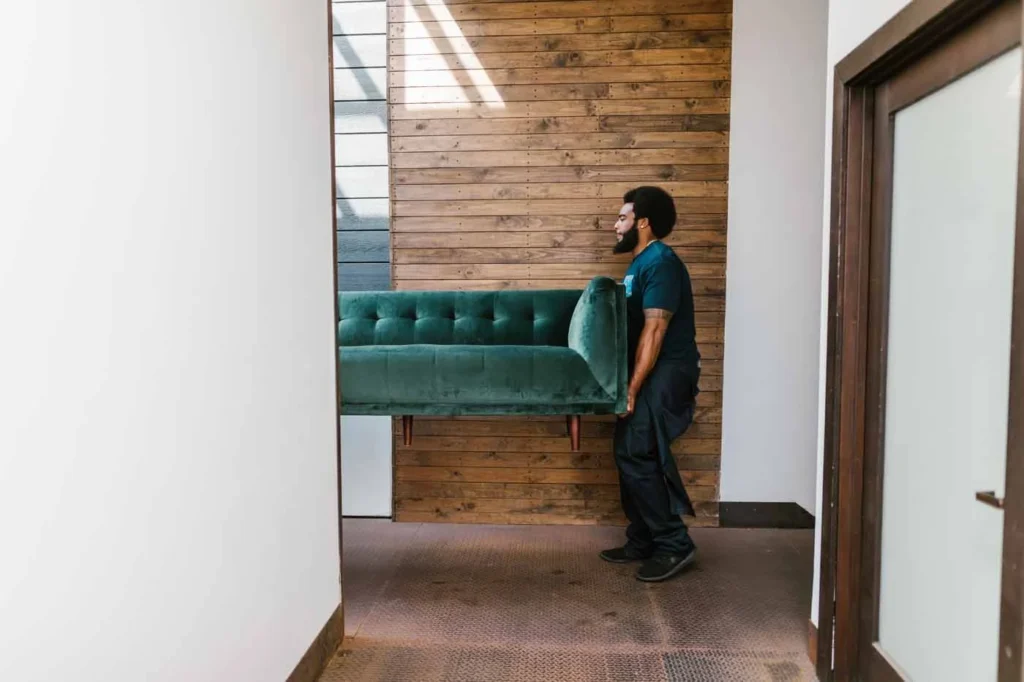 A mover carrying a sofa indoors during a house move